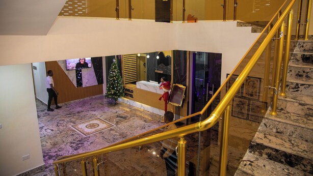 A hotel lobby with a Christmas tree, a reception desk, and a staircase with golden railings.