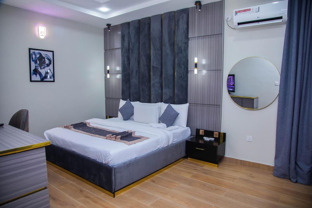 A modern bedroom with a bed, bedside tables, a desk, and a wall-mounted air conditioner.