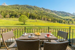En balkon med fletningsmøbler, et bord med et fad croissanter og en smuk bjergudsigt.