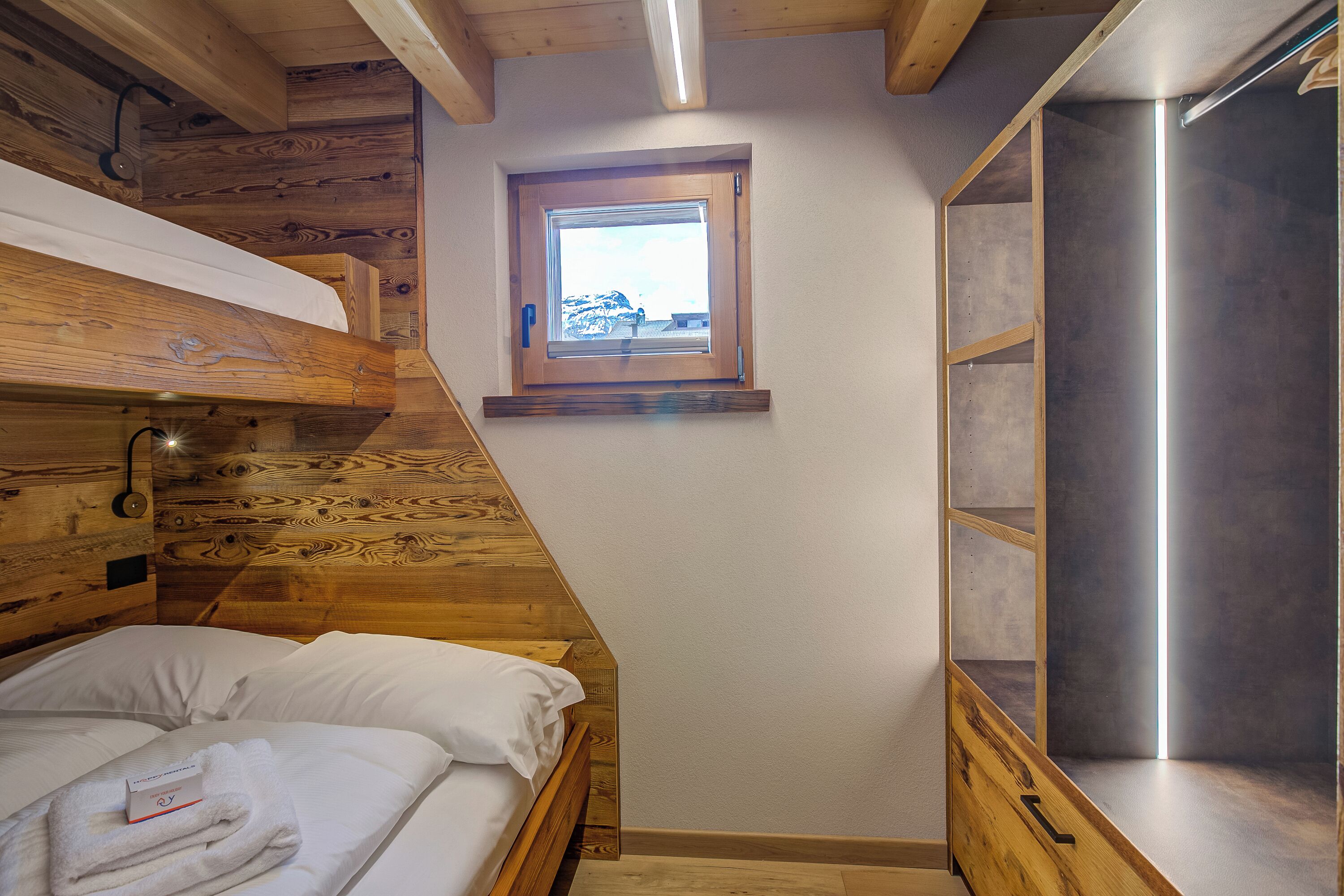 A bedroom with a bunk bed, a small window, and a built-in shelf.