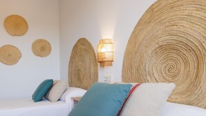 Un dormitorio con cama, dos almohadas, mesita de noche y lámpara de pared.
