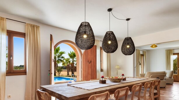 Un comedor amplio con una larga mesa de madera, seis sillas y lámparas colgantes tejidas.