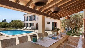 Un área de piscina exterior con una pérgola de madera, sillas de descanso y una mesa de comedor con sillas de mimbre.