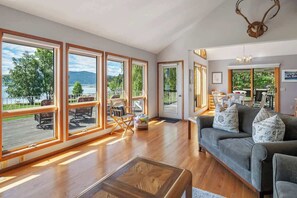A spacious living room with large windows, a grey sofa, and a wooden coffee table.