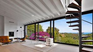 Un intérieur moderne avec une grande fenêtre, un escalier en colimaçon et une vue sur la verdure et un paysage lointain.
