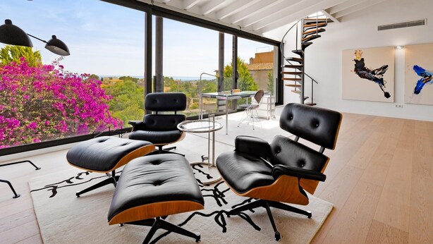 Un salon moderne avec une grande fenêtre, des fauteuils en cuir noir, une table en verre et un escalier en colimaçon.