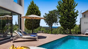 Un espace piscine extérieur moderne, doté de chaises longues et d’un panier de fruits.