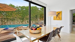 Un espace repas moderne avec une table en verre, des chaises blanches et un saladier rempli de fruits.