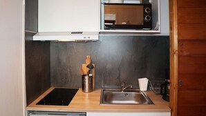 Una cucina compatta con forno a microonde integrato, lavello in acciaio inossidabile e un piccolo frigorifero.