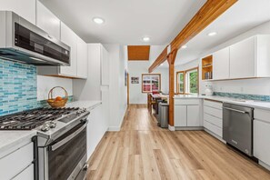 A modern kitchen with white cabinets, a stainless steel stove, and a wooden floor.
