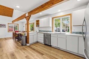 Une cuisine moderne avec des poutres en bois, des meubles blancs et une grande fenĂȘtre.