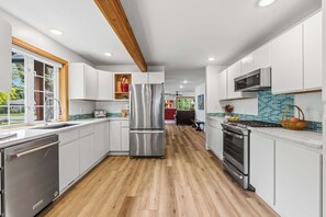 Eine moderne KĂŒche mit weiĂen SchrĂ€nken, EdelstahlgerĂ€ten und einer Holzbalkendecke.