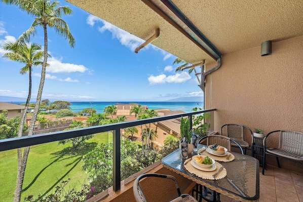 A balcony with a table set for dining, overlooking a scenic view of the ocean and a golf course. - Perfect Maui Getaway Condo w Ocean Views-Kahana Villa F405 (Lahaina)