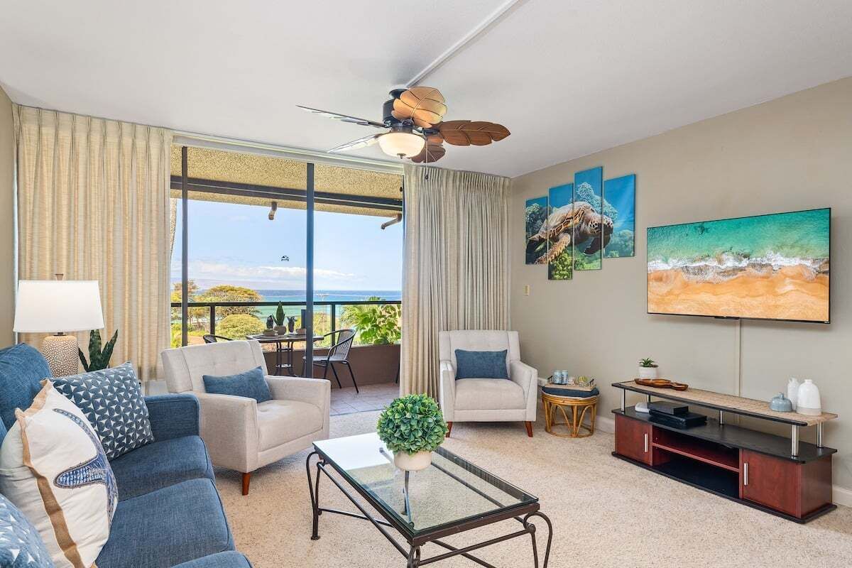 Ein Wohnzimmer mit Meerblick, einem Deckenventilator und einem Flachbildfernseher.