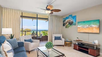 Ein Wohnzimmer mit Meerblick, einem Deckenventilator und einem Flachbildfernseher.