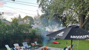 An outdoor patio with a grill, lounge chairs, and a fire pit. - Private backyard, fire pit, bbq, beach, boats and entertainment…fun! (Lake Geneva)