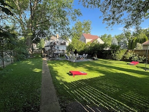 A well-maintained backyard with a lawn, a patio area with chairs, and a red table.