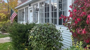 A white house with multiple windows, a front door, and an American flag. - Private backyard, fire pit, bbq, beach, boats and entertainment…fun! (Lake Geneva)