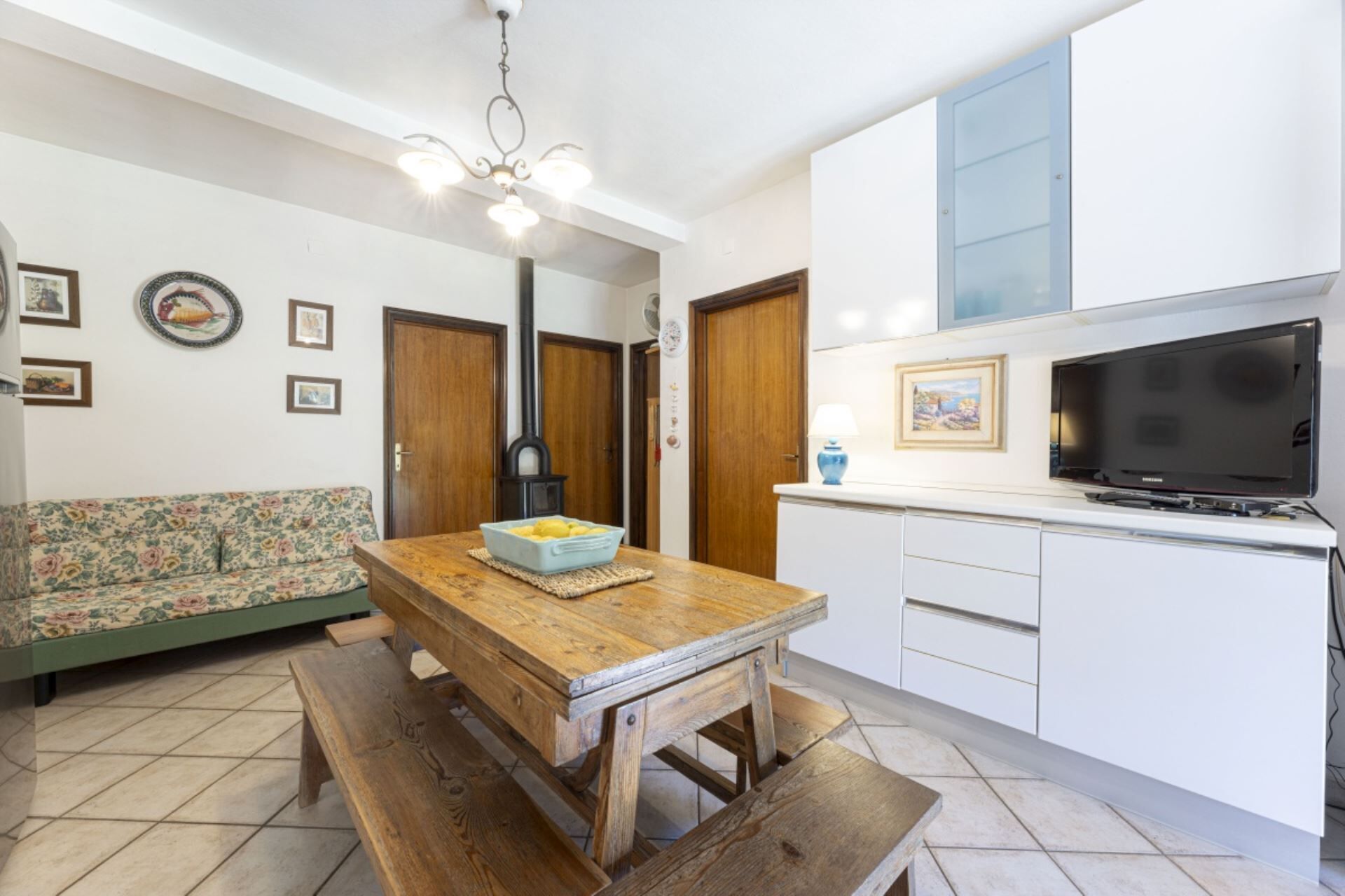 A compact kitchen with a wooden table, bench, and a built-in TV.