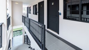 Ein moderner Hotelkorridor mit schwarzen, nummerierten Türen 4 und 5, einem Balkon mit Metallgeländer und einem gemusterten Boden.