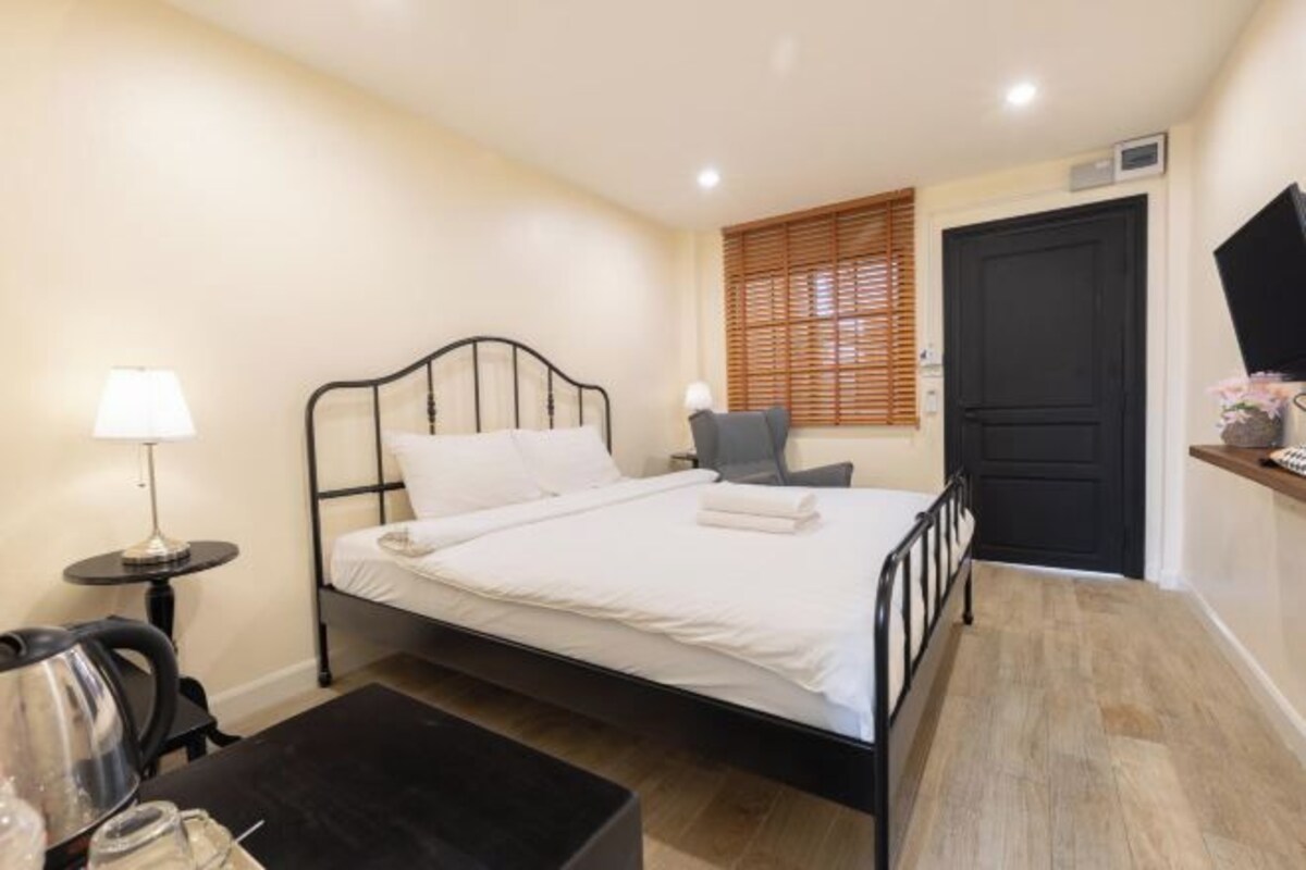 Een slaapkamer met een bed, nachtkastje, lamp, stoel en een deur.