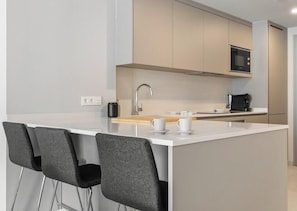 A modern kitchen with a central island, bar stools, a microwave, and a coffee maker.
