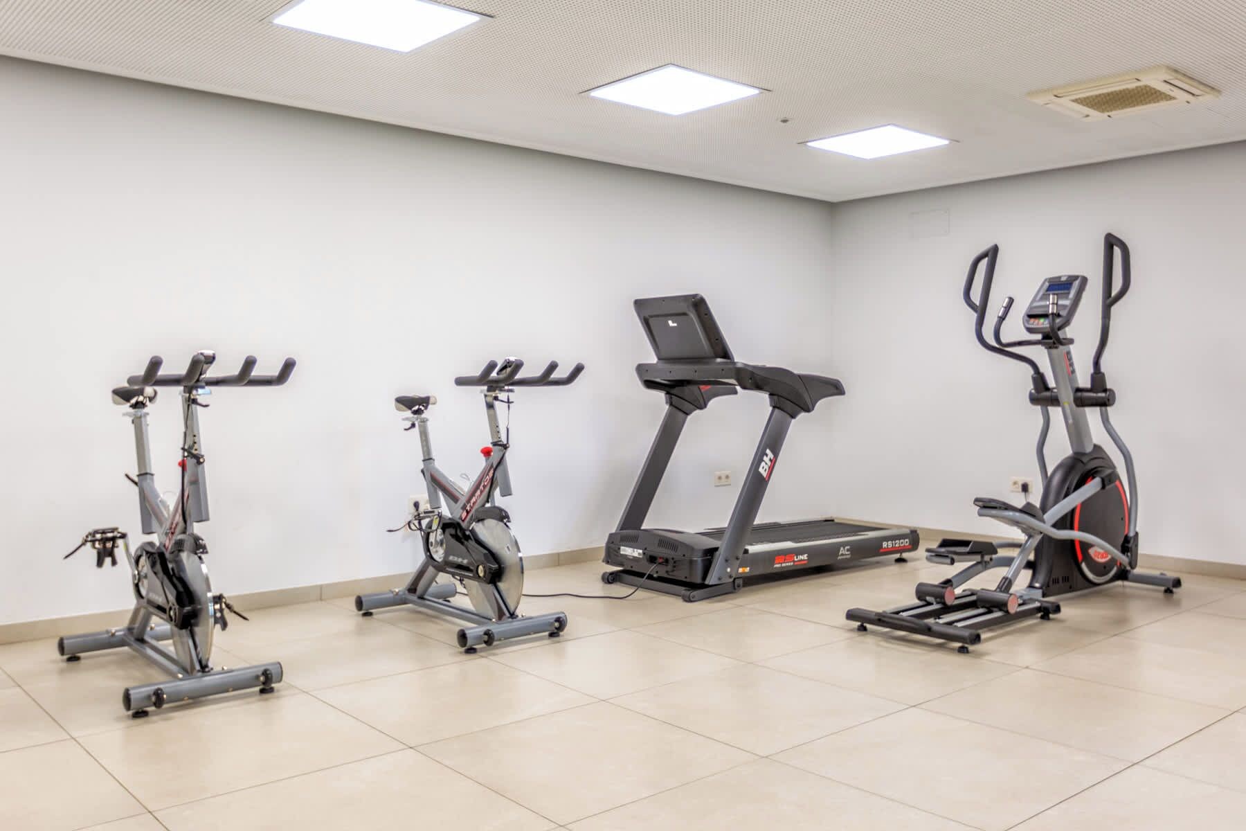A fitness room with four exercise bikes and a treadmill.