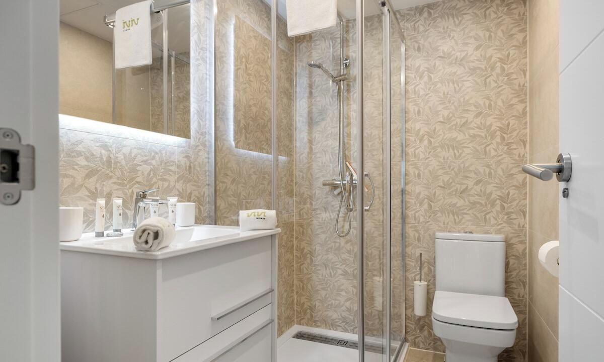 A modern bathroom with a glass shower enclosure, a toilet, and a vanity with toiletries.