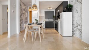 Eine moderne Küche mit Essbereich, ausgestattet mit einem weißen Kühlschrank, schwarzen Schränken und einer gefliesten Spritzschutzwand.