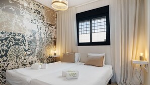 Ein Hotelzimmer mit einem großen Bett, zwei Nachttischen mit Lampen, einem Fenster mit Vorhängen und einer Wand mit Muster.