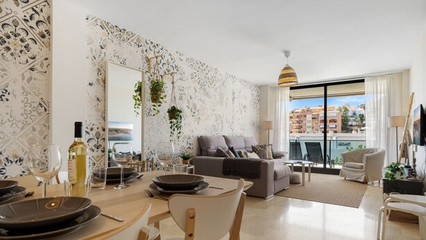 Ein modernes Wohnzimmer mit Essbereich, einem grauen Sofa und einem Balkon mit Blick auf Gebäude.