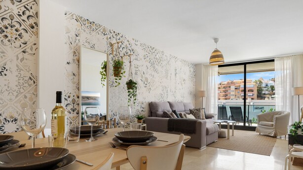 Un salon moderne comprenant un coin repas, un canapé gris et un balcon offrant une vue sur les immeubles.