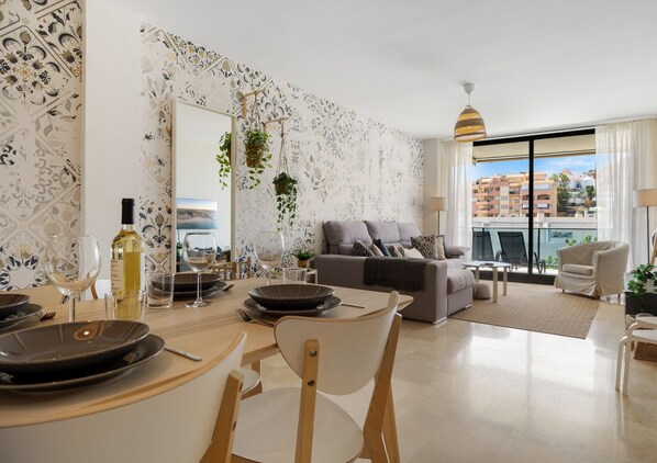 Un salon moderne comprenant un coin repas, un canapé gris et un balcon offrant une vue sur les immeubles.