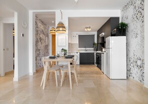Une cuisine moderne avec un coin repas, comprenant un réfrigérateur blanc, des armoires noires et un crédence décorée.