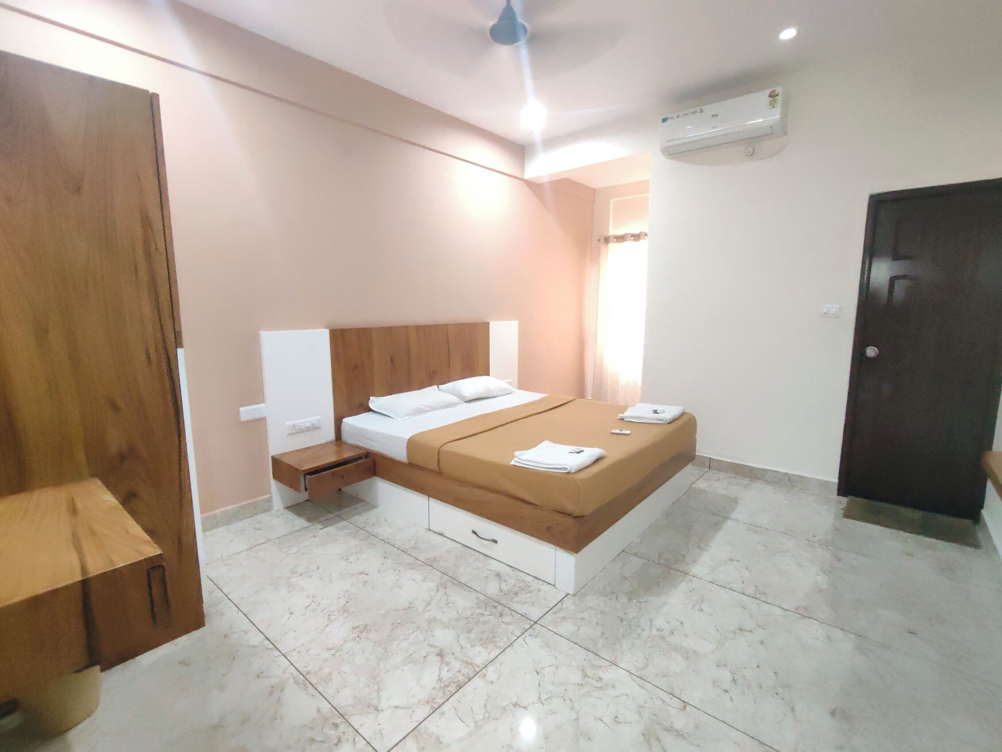 Une chambre à coucher comprenant un lit, des tables de chevet, une armoire en bois, un ventilateur de plafond et un appareil de climatisation.