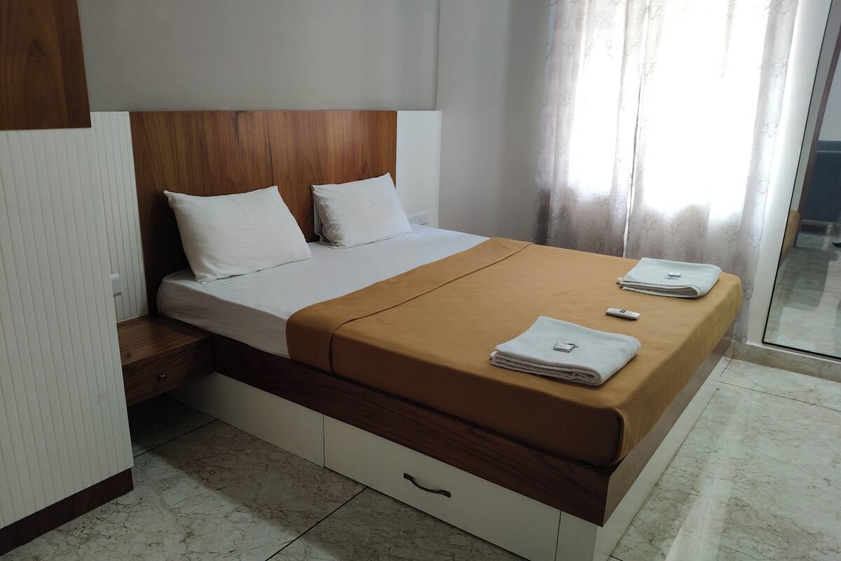 A neatly made bed with a brown bedspread, white pillows, and a folded towel on the side.