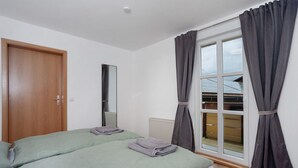 Un dormitorio con dos camas, una puerta de madera, un ventanal con cortinas y un radiador.