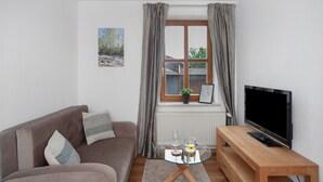 Una sala de estar con un sofá, una mesa de centro de vidrio, un televisor y una ventana con cortinas.