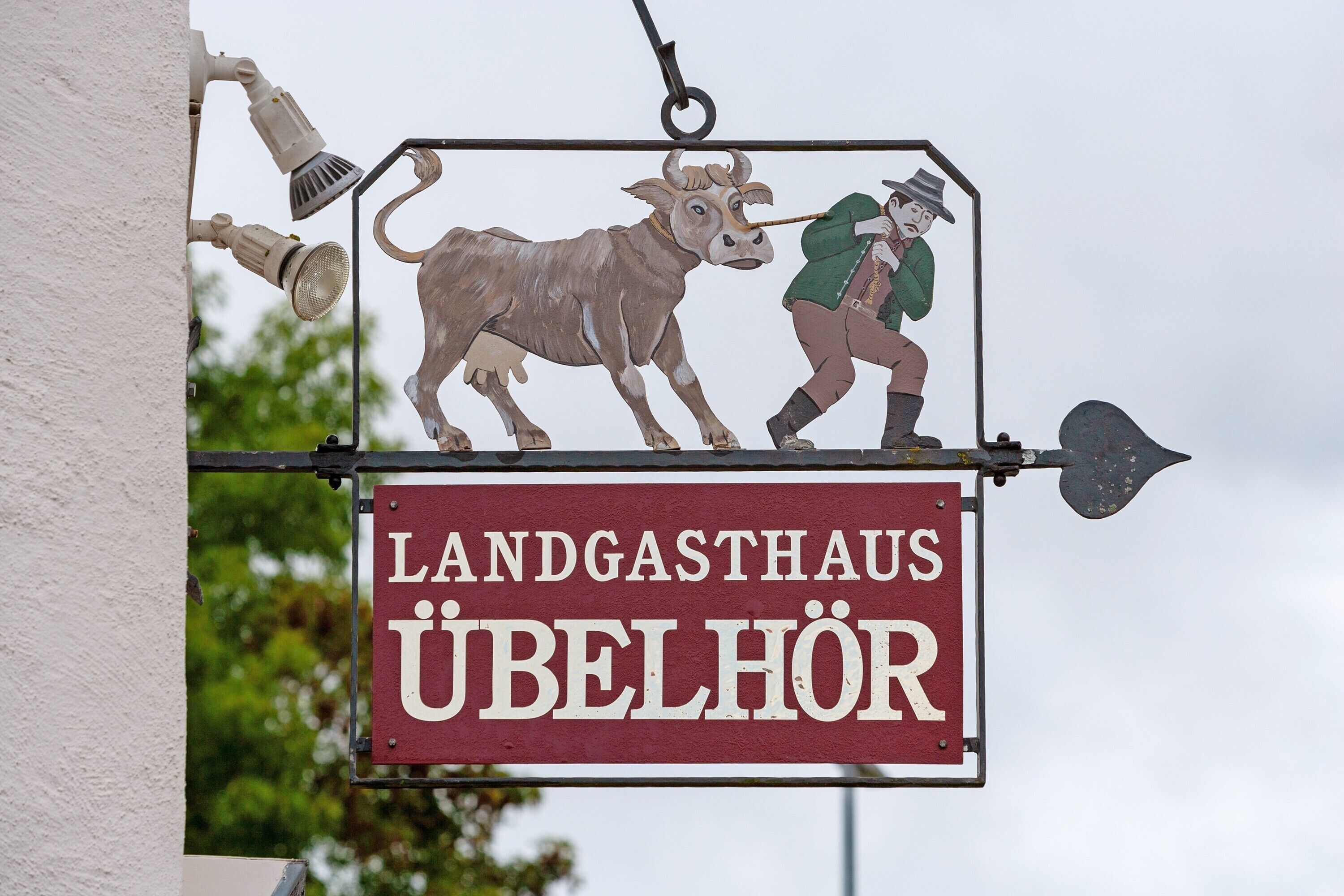 Ein Schild mit einer Kuh und einem Mann, mit dem Text 'LANDGASTHAUS ÜBELHÖR'.