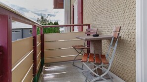 Un balcón con mesa y sillas, barandilla metálica y pared con textura.