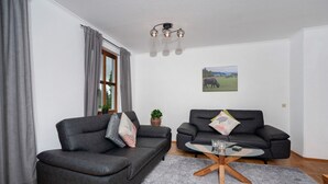 Een woonkamer met twee donkere banken, een ronde salontafel, een grijze vloerkleed, een raam met gordijnen, een wandlamp en een ingelijste foto.