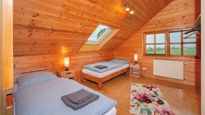 A wooden cabin bedroom with two beds, a skylight, and a window with a view.