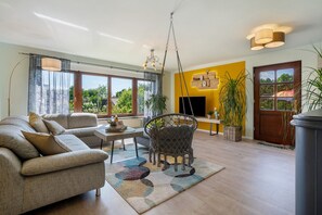 Una sala de estar moderna con un sofá, una mesa de centro y una silla colgante. Hay una chimenea, un televisor y un ventanal grande.