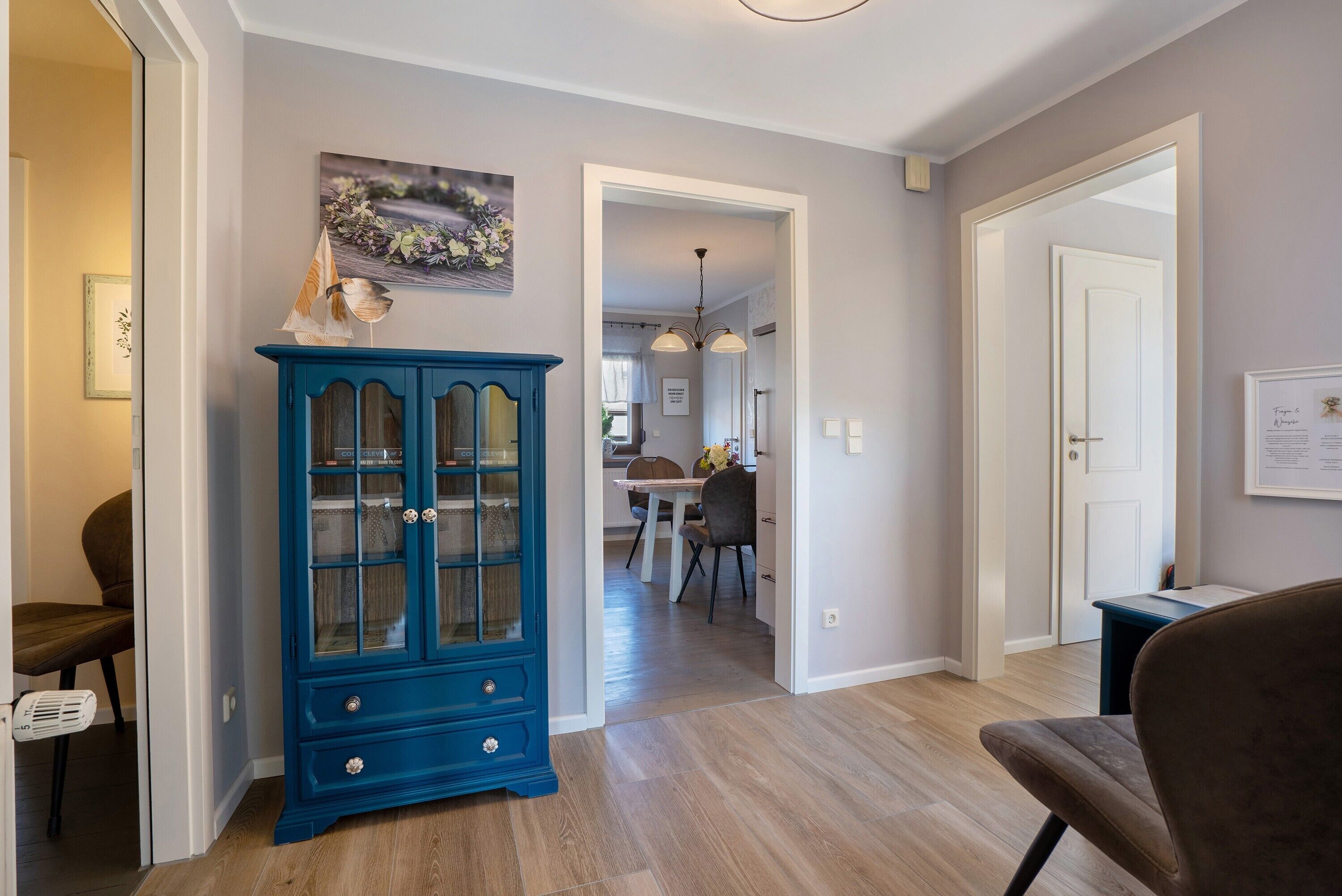 A hallway with a blue cabinet, a dining area, and a door leading to another room.