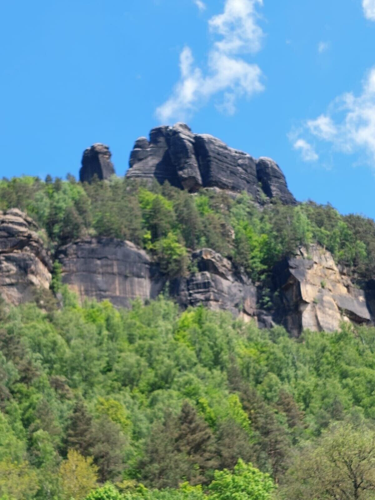 A mountainous landscape with prominent rock formations and dense green forest.