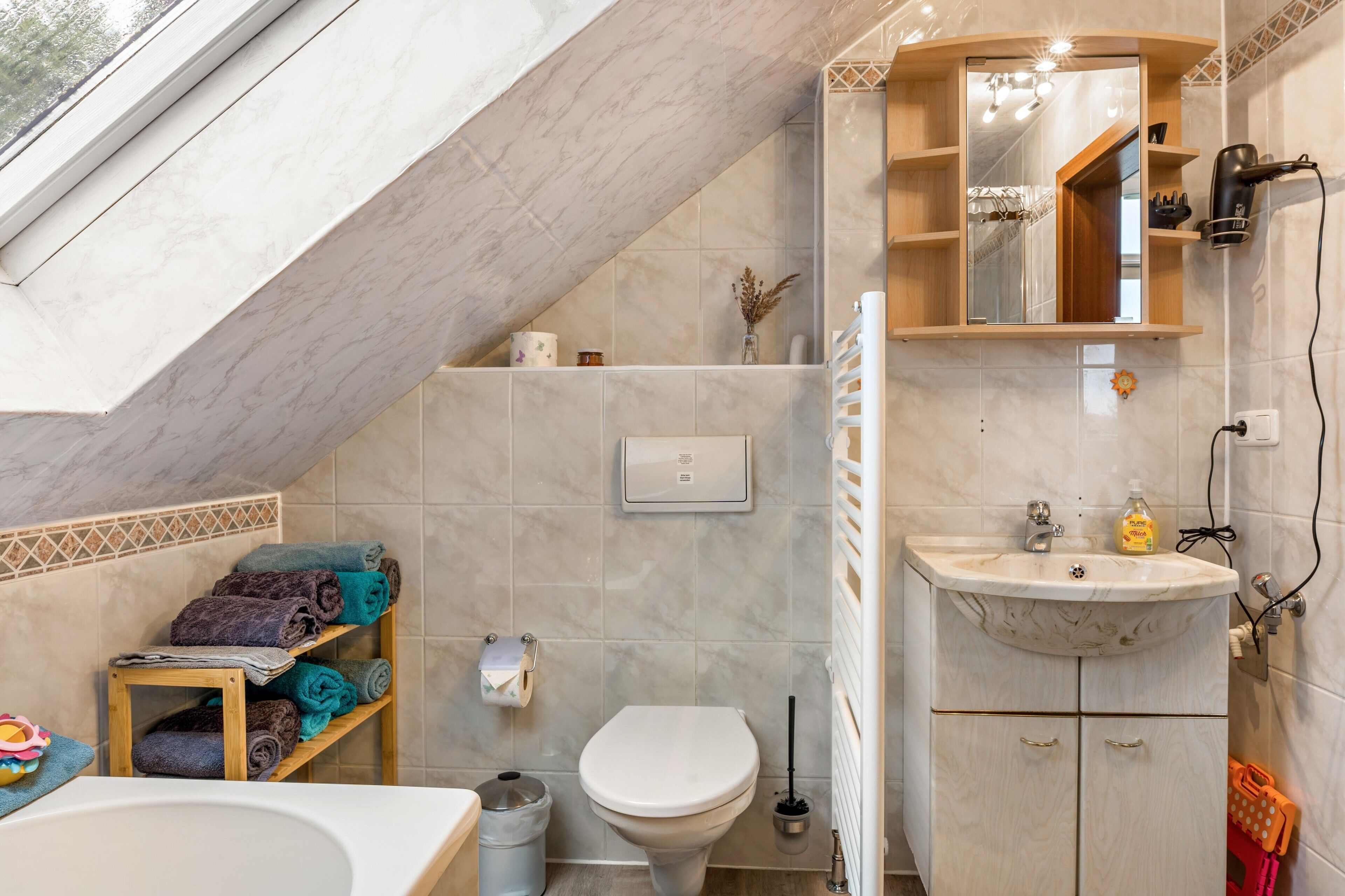 Une salle de bain avec un puits de lumière, des toilettes, un lavabo, un miroir et une étagère avec des serviettes.