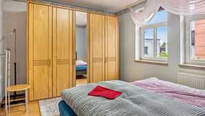 Ein Schlafzimmer mit einem Bett, einem Holzschrank, einem Fenster und einer Heizung.