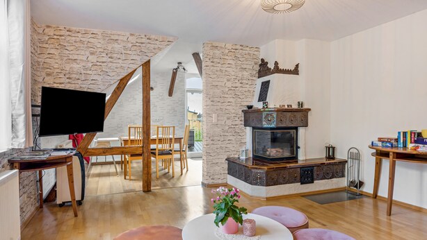Ein Wohnzimmer mit Steinwand, Kamin, Fernseher, Holzmöbeln und Blick ins Freie.