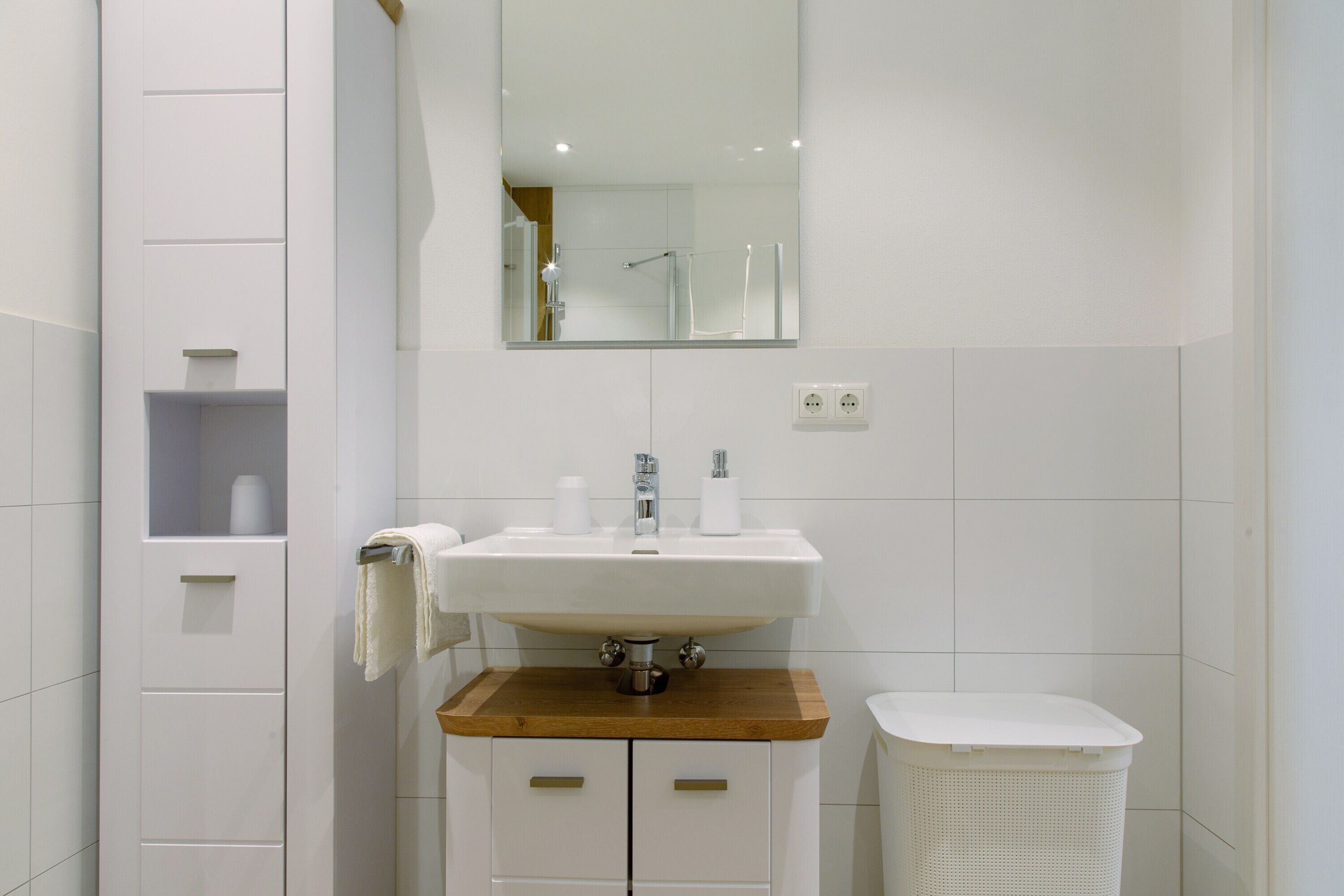 Une salle de bain avec un lavabo blanc, un plan de travail en bois et un panier à linge blanc.