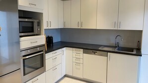 Moderni keittiö, jossa on valkoiset kaapit, ruostumattomasta teräksestä valmistetut kodinkoneet, musta työtaso ja sisäänrakennettu astianpesukone.